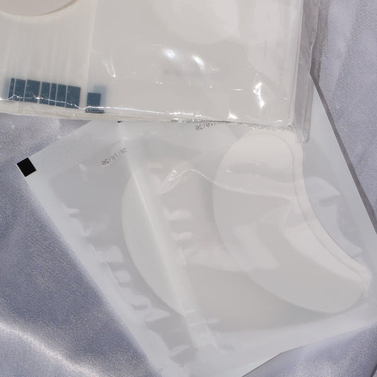 Close-up of white crescent-shaped lash extension eye pads in individual packaging.