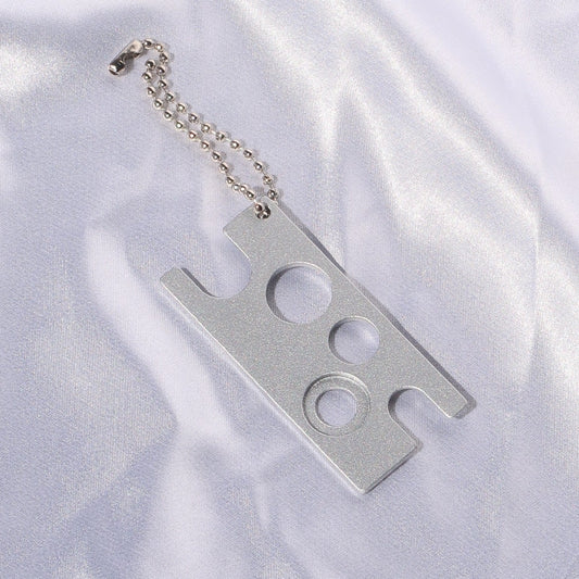 Silver lash glue nozzle opener with multiple openings and an attached ball chain.