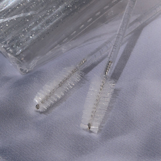 Close-up of lash spoolie brushes with white bristles and clear glitter handles.